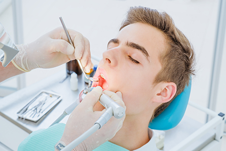 A dental patient receiving treatment while seated in a dentist s chair, with a dental practitioner performing the procedure.