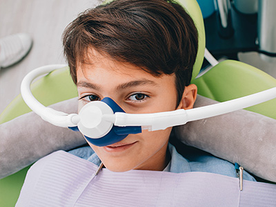 The image shows a young man wearing an oxygen mask while sitting in a dental chair.