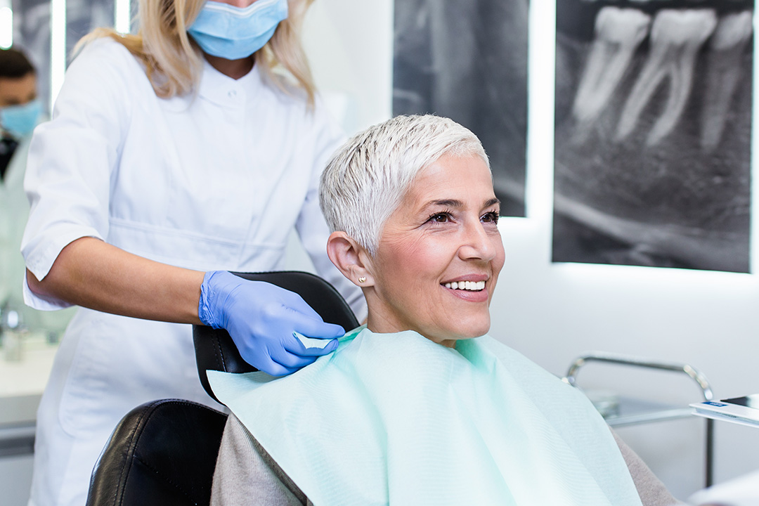 A woman receiving a haircut from a stylist while seated in a dental chair.