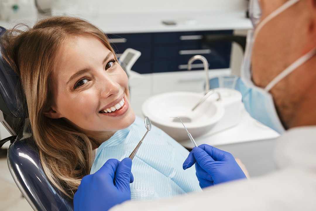 A woman sitting in a dental chair receiving treatment from a dentist, with a smiling expression on her face.