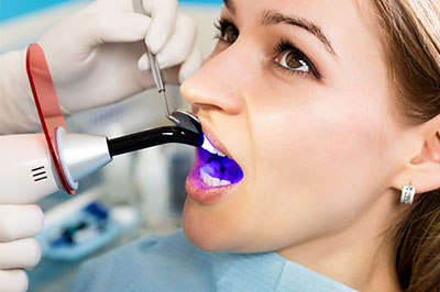 A woman receiving dental treatment with a device that appears to be a dental implant tool, surrounded by medical equipment and staff.