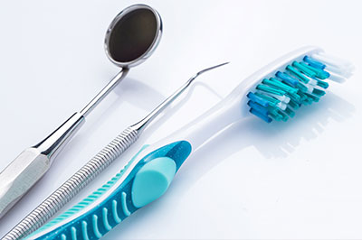 The image shows dental tools including a toothbrush with blue bristles, a pair of scissors, and other dental instruments on a white surface.