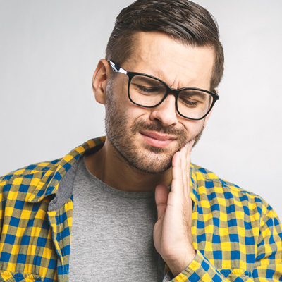 The image shows a young man with glasses, wearing a blue plaid shirt and a light-colored beanie, with his hand on his chin, seemingly deep in thought or concern.