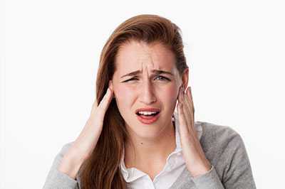 A young woman with her hand on her head, possibly indicating discomfort or pain, against a white background.