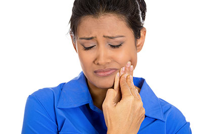 The image shows a woman with her eyes closed, holding her face with both hands, seemingly in pain or distress, while looking downwards.