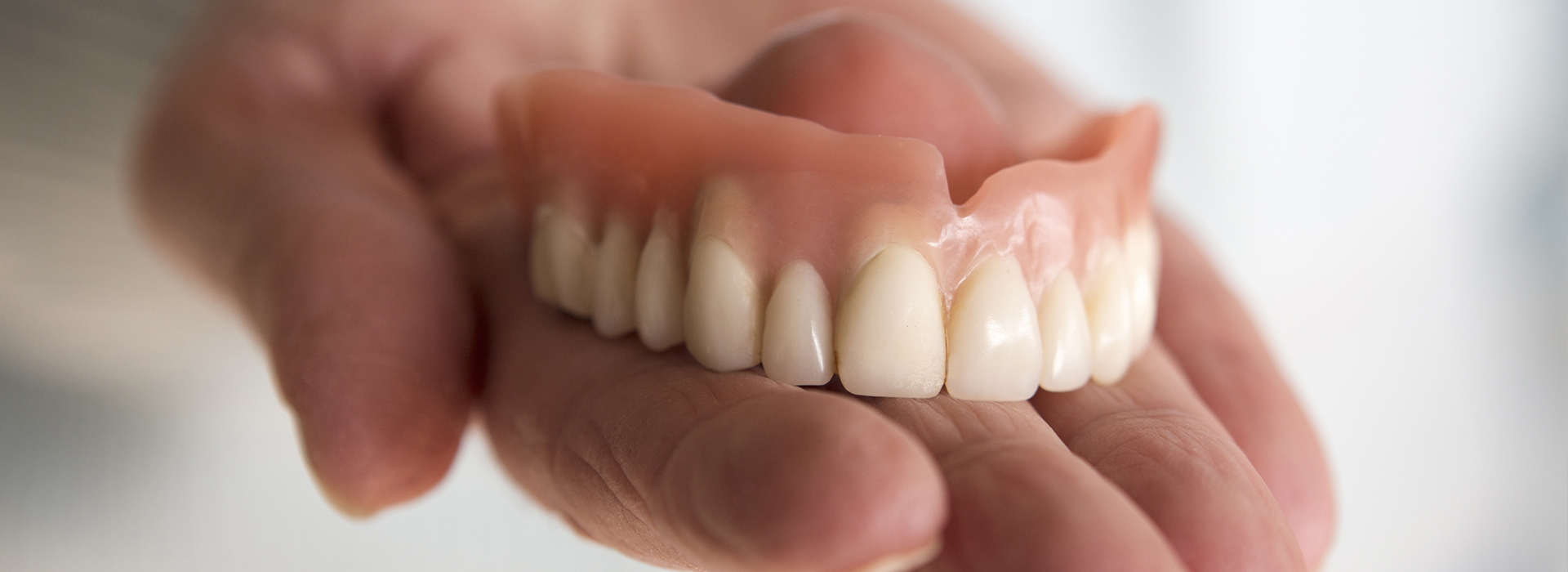 An adult hand holding a set of dentures against a blurred background.