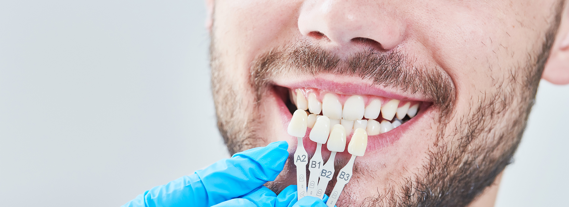 The image shows a man with a toothy smile wearing a face mask and holding dental instruments, likely a dentist at work.