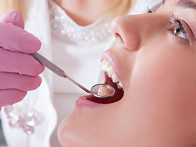 An image showing a person receiving dental care with a dentist working on their mouth using dental tools, set against a professional backdrop with medical equipment.