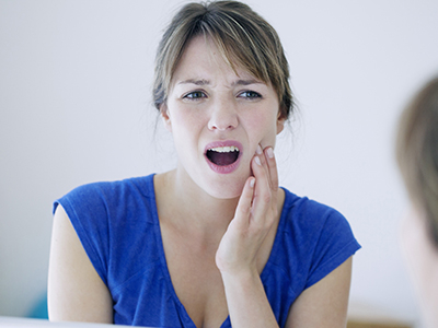 The image depicts a woman with her hand on her face, looking into a mirror, with an expression of concern or worry.