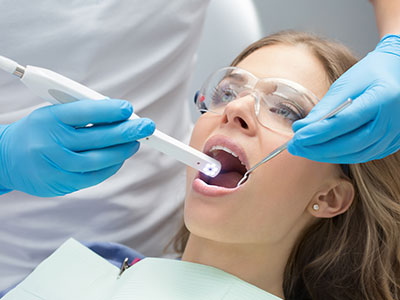 A dental professional is examining a patient s teeth using an electronic device, with the patient sitting comfortably in a dental chair.