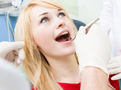 A young woman receiving dental care with a smile, seated in a dental chair while a dental professional works on her teeth.