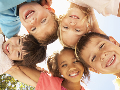 A group of children posing together with smiles on their faces, under a bright sky.
