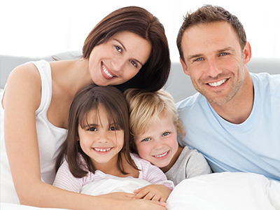 A family of four adults and three children posing together on a bed with a happy expression.