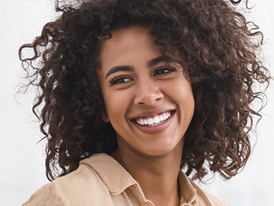 The image shows a smiling woman with curly hair, wearing a light-colored top, against a neutral background.